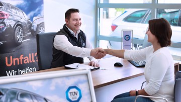 Ein TÜV SÜD Mitarbeiter im Autohaus Weeber schüttelt Kundin die Hand