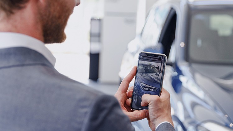 Kundenbindung im Aftersales: Nextlane setzt neue Maßstäbe Mann blickt auf Smartphone, im Hintergrund ein Auto